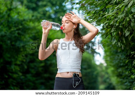 Woman athlete takes a break. Drinking water, out on a run in the park