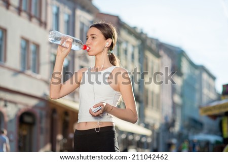 Sporty woman drinking water. Runner have a break with bottle of water. Female fitness jogger training outside for healthy lifestyle.