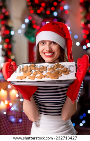 Happy young woman holding pan with ginger cookies on festive lighting background