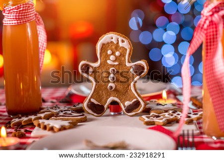 Sweet Christmas decorated table with ginger manikin cookies, candles, drinks and lights on background on red checkered tablecloth