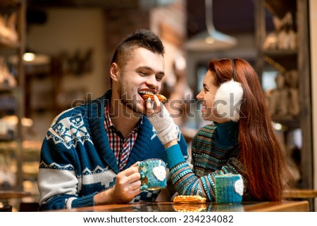 Young loving couple dressed in blue sweater sitting with knitted coffee cups in the cafe in winter