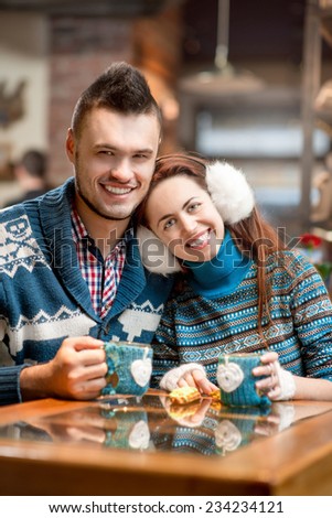 Young loving couple dressed in blue sweater sitting with knitted coffee cups in the cafe in winter