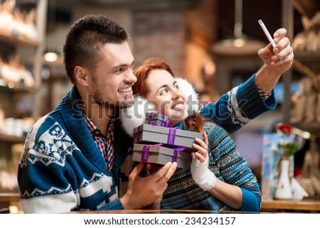 Young couple making selfie photo with gift boxes at the cafe in winter