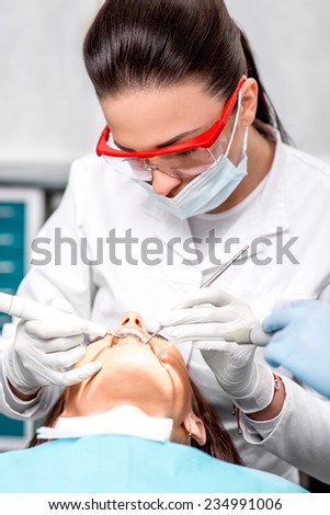 Dentist making professional teeth cleaning female young patient at the dental office