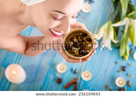 Smiling young woman with cup of herbal tea in bath towel in spa salon. Herbal treatment.