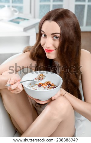 Young positive woman eating granola breakfast on the couch at home