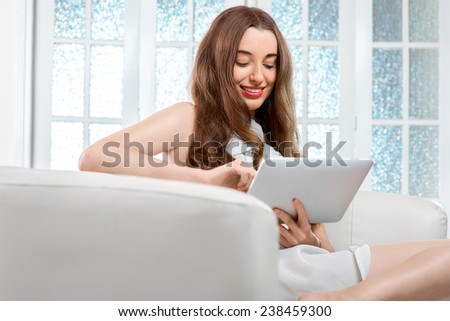 Smiling young woman using tablet sitting on the couch at home