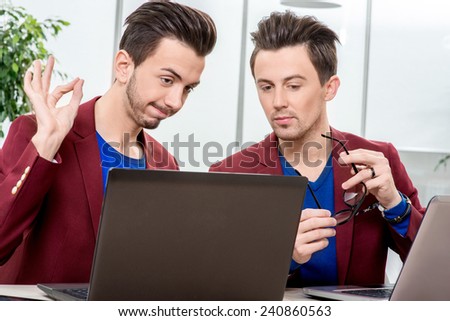 Two brothers twins in red jackets working with laptops and smart phones at the office. Family business