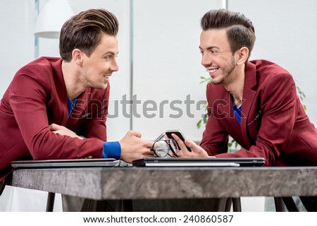 Two brothers twins in red jackets discussing something with smart phones at the office table