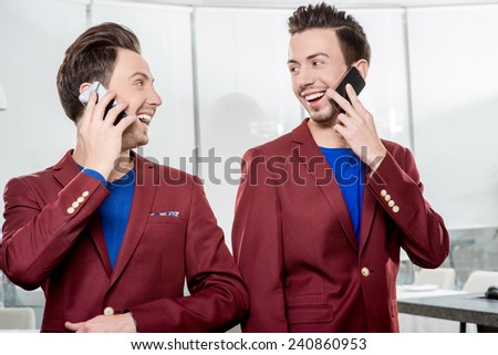Friendly business brothers twins in red jackets using mobile phone in white office