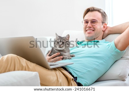 Handsome man with cat and laptop laying on the couch at home.