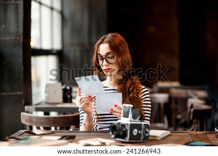 Young woman photographer looking at the printed photos with old 6x6 frame camera sitting in the loft design interior