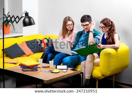 Three young friends or students reading colorful books on the yellow couch at home
