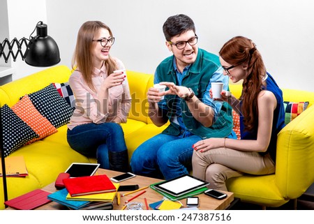 Friends talking and laughing with coffee cups on the yellow couch