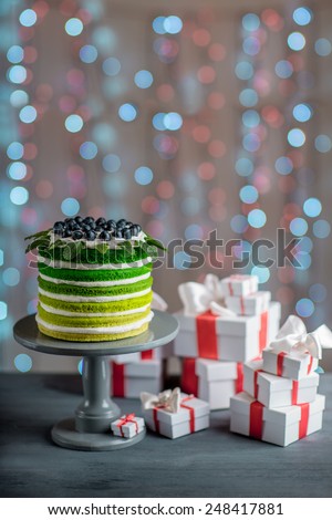 Nice sponge happy birthday cake with mascarpone and grapes with on the cake stand with gift boxes on festive light bokeh background