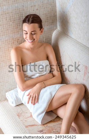 Young woman in white towel sitting and enjoying in Roman sauna