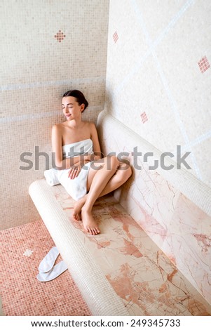 Young woman in white towel sitting and enjoying in Roman sauna
