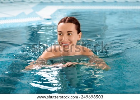 Young smling woman swimming in the swimming pool at the hotel spa