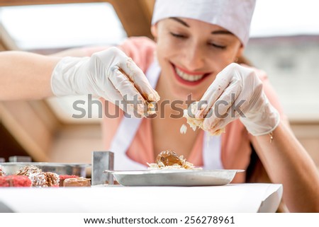 Young smiling woman chef dressed in white pinafore making handmade chocolate candy in the cafe