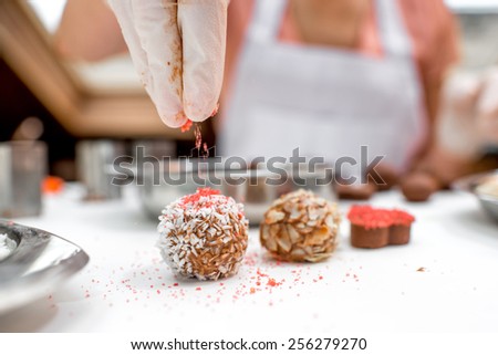Young woman making and decorating chocolate candy with coconade, red sugar and almonds on the white table