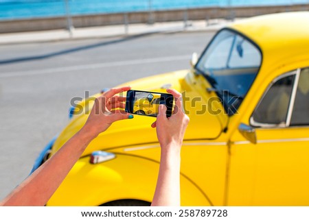 Woman photographing with smart phone old yellow car on the street