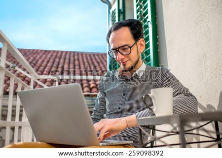 Man working with laptop on the balcony at home with green window shutters.
