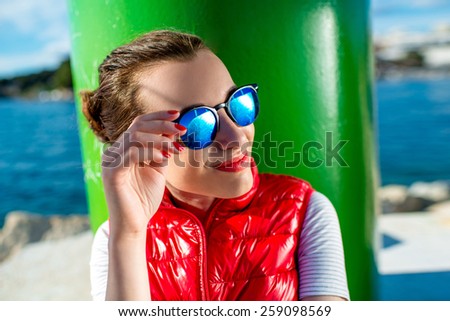 Sport woman puitting on sunglasses while sitting near the lighthouse on the beach