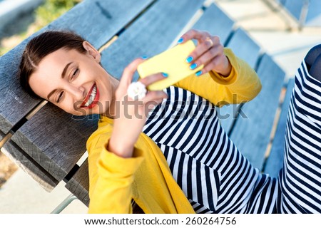 Woman in yellow having video call or taking selfie photo with yellow phone on wooden sunbed