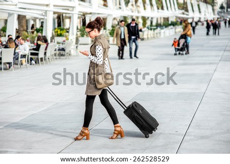 Young woman with travel bag and phone walking at the promenade in Split cty in Croatia