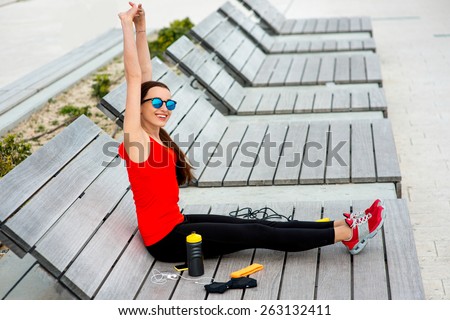Young sporty woman having exercise on the wooden sunbed with jump rope, gloves and drink bottle on background