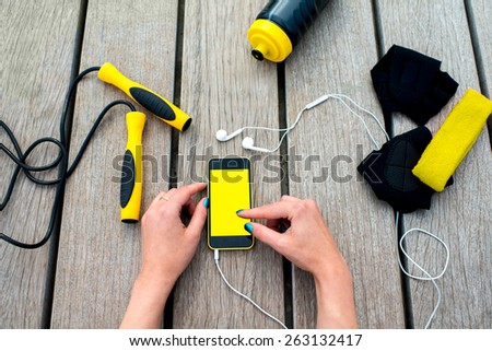 Using mobile phone with empty screen on the wooden desk surrounded with sport equipment. Sport mobile application concept