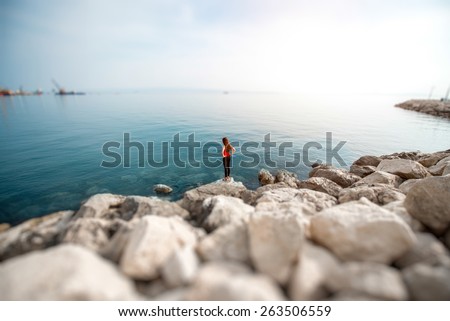 Alone sport woman in red standing on the rocky beach. General plan