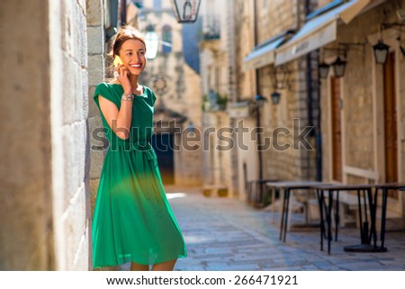 Young woman in beautiful green dress using mobile phone walking on the old city street in Dubrovnik, Croatia