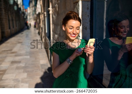 Young woman in beautiful green dress using mobile phone standing near the windoow on the old city street in Dubrovnik, Croatia