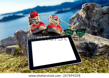 Digital tablet with empty screen with shoes and glasses on the mountain. Hiking or sports application concept