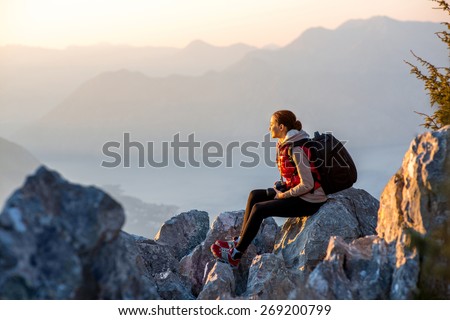 Young traveler photographer with photo camera and backpack sitting on the top of mountain and looking on the sunset