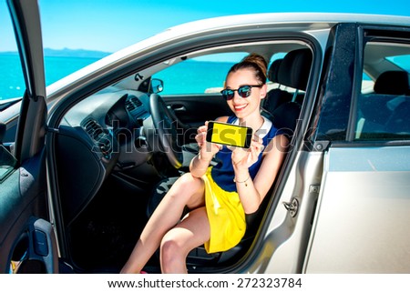 Young and cute woman showing phone screen sitting in the car. Navigation or travel phone program concept.