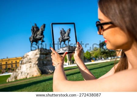 Young woman tourist photographing with digital tablet Skanderbeg monument in Tirana, Albania.