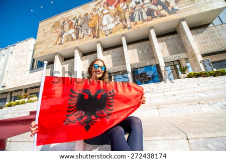 Young woman patriot with Albanian flag sitting in front of National museum in Tirana city