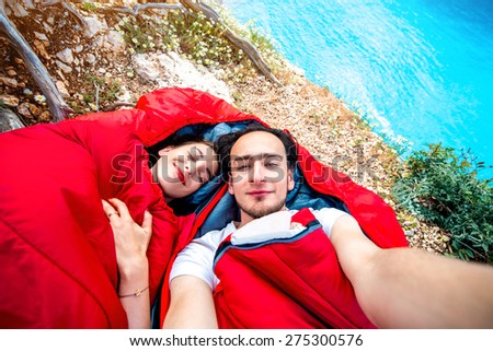Young couple lying in red sleeping bags near the sea