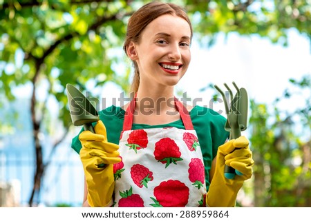 Portrait of a young woman gardener with apron and gardening tools outdoors on the green background