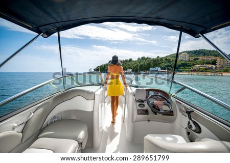 Young and pretty woman in yellow swimsuit standing on the yacht floating in the sea with view on the island