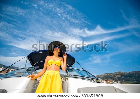 Young and pretty woman in yellow swimsuit standing in the yacht floating in the sea. Luxury summer recreation