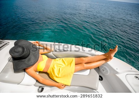 Young and pretty woman in yellow swimsuit with big hat relaxing on the yacht floating in the sea. Luxury summer recreation