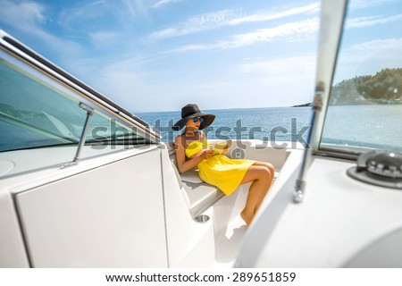 Young woman in yellow swimsuit and skirt reading with digital tablet on the yacht floating in the sea