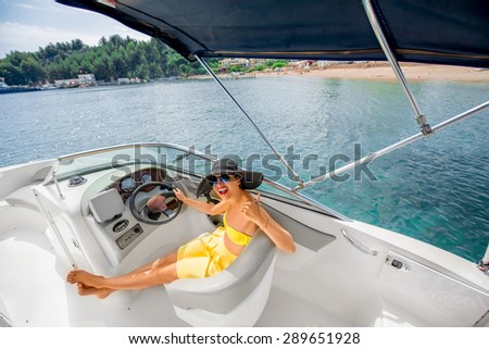 Young and pretty woman in yellow skirt and swimsuit with hat and sunglasses driving luxury yacht in the sea. Top view with copy space