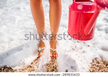 Woman\'s legs in the slippers with pink watering can on the beach