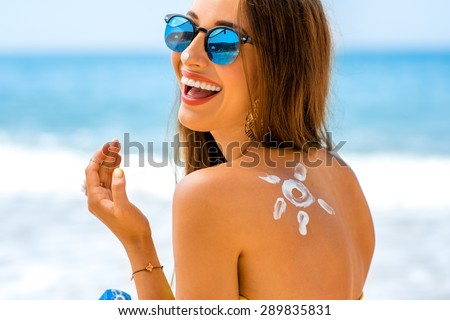 Young woman with sun shape on the shoulder holding sun cream bottle on the beach