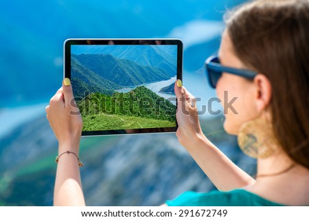Young woman photographing beautiful landscape with digital tablet standing on the top of mountain
