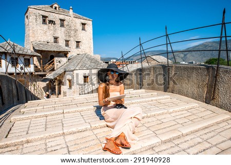 Female tourist using digital tablet sitting on the old bridge in Mostar city in Bosnia and Herzegovina